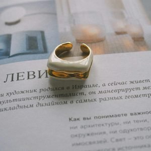A minimalist gold ring placed on an open magazine page with artistic text in Russian.