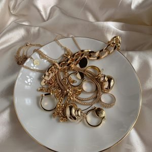 Stylish gold rings and necklaces elegantly displayed on a saucer with a silk background.